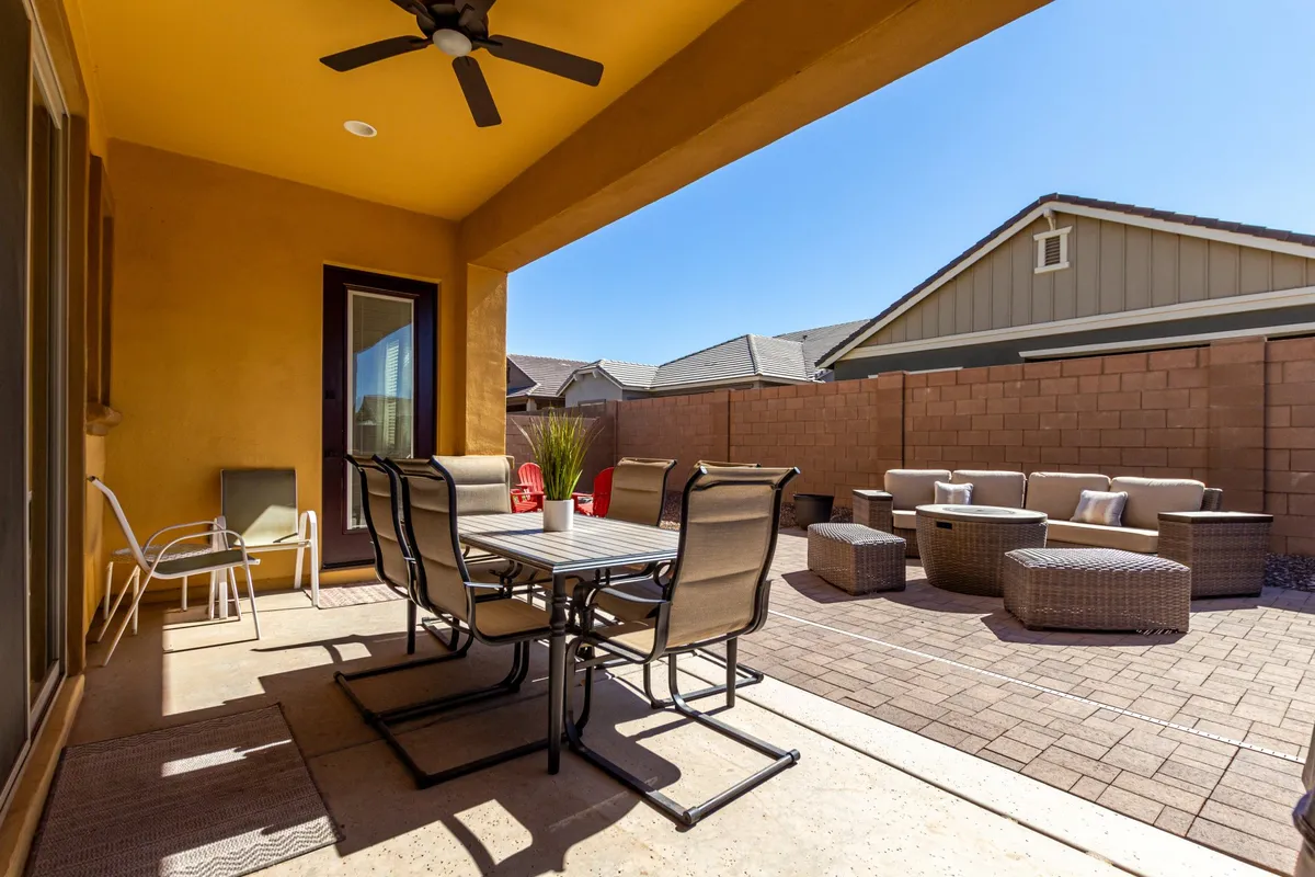 An outdoor dining table and lounge seating area beneath a ceiling fan, set up on a patio. The setting is ideal for both active mornings and relaxed sunset meals, and the mood is social and inviting.