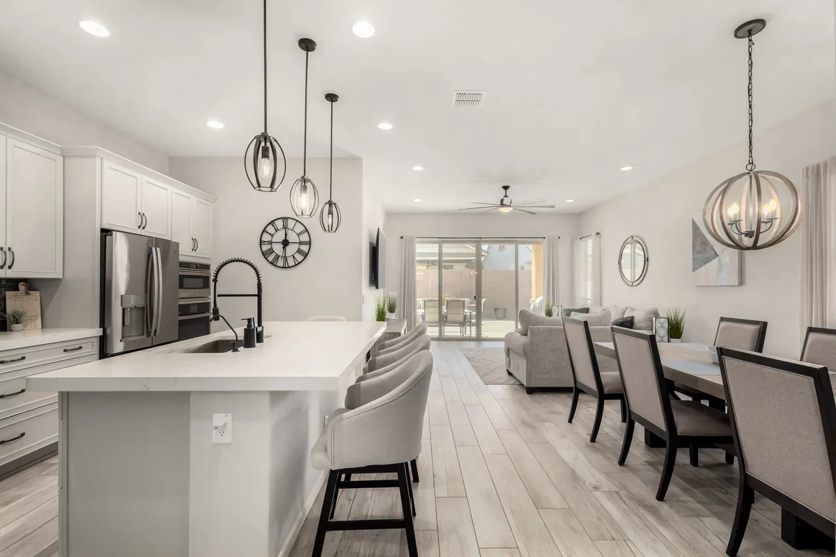 A bright, airy view of a contemporary kitchen island, dining area, and large windows that flood the space with natural light. Pendant lighting and modern finishes create an inviting atmosphere for both casual family meals and larger gatherings.