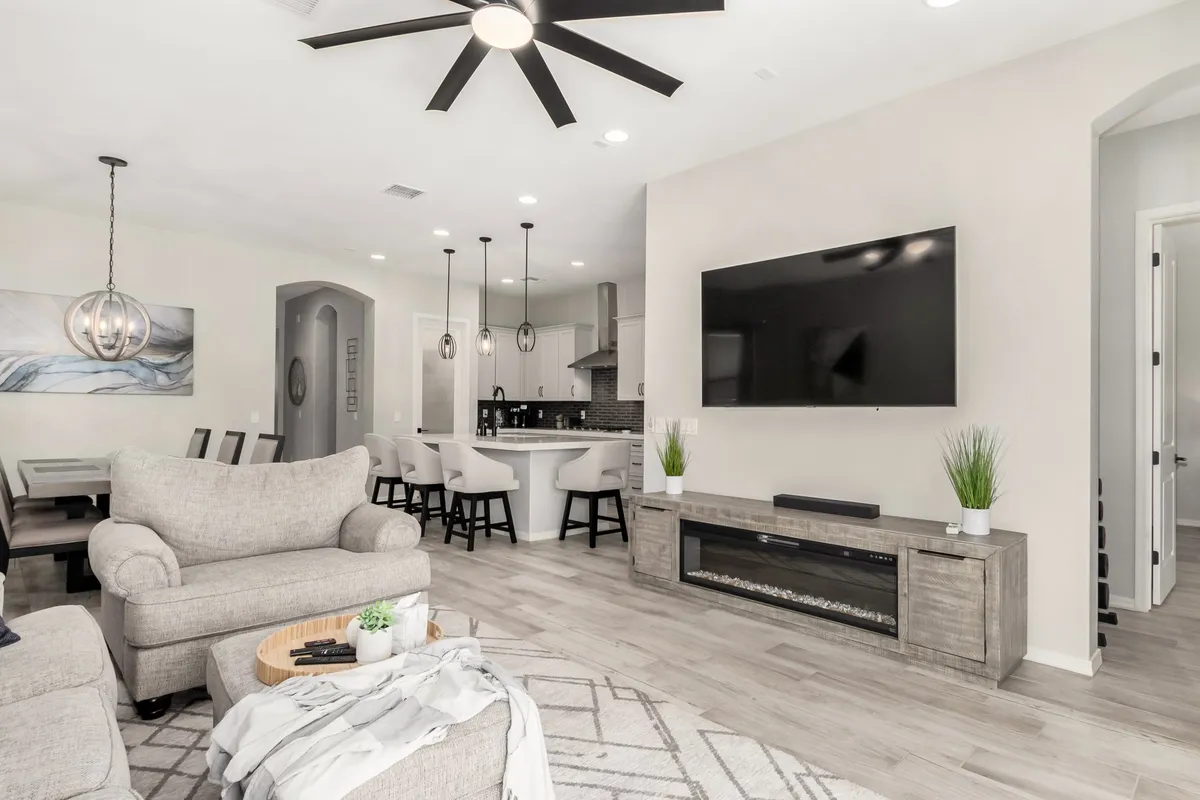 A comfortable and modern living space that features a sofa, a dining area, a TV, a kitchen island, and a ceiling fan—all within view. The arrangement encourages interaction across the different areas, reinforcing the theme of togetherness and flexibility for various activities, from entertaining to relaxing.