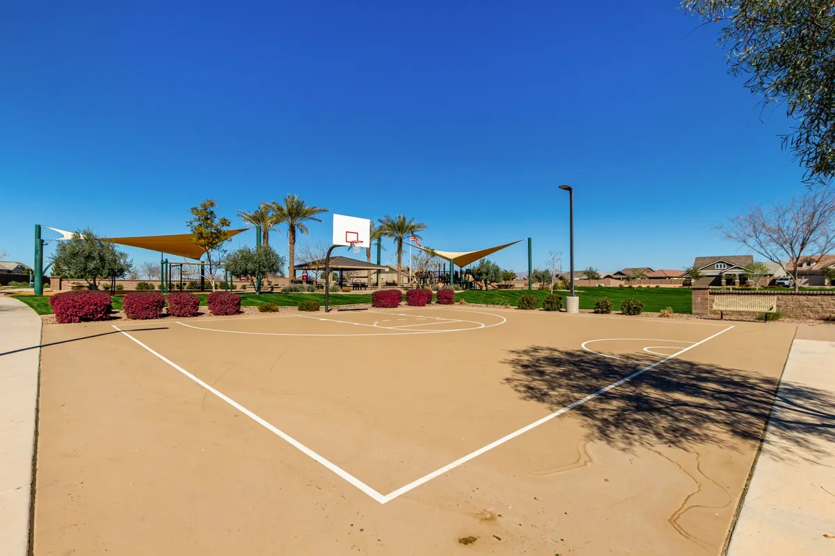 A neighborhood park with a full basketball court, modern playground equipment, and lush landscaping. The area is bustling with activity, capturing families enjoying the space, children playing, and others engaged in a friendly basketball game.