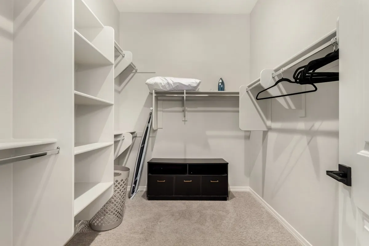 An organized closet space with shelves, hanging clothes, a storage bin, and clean flooring. The area is calm and tidy, ideal for organizing belongings and ensuring ample storage.