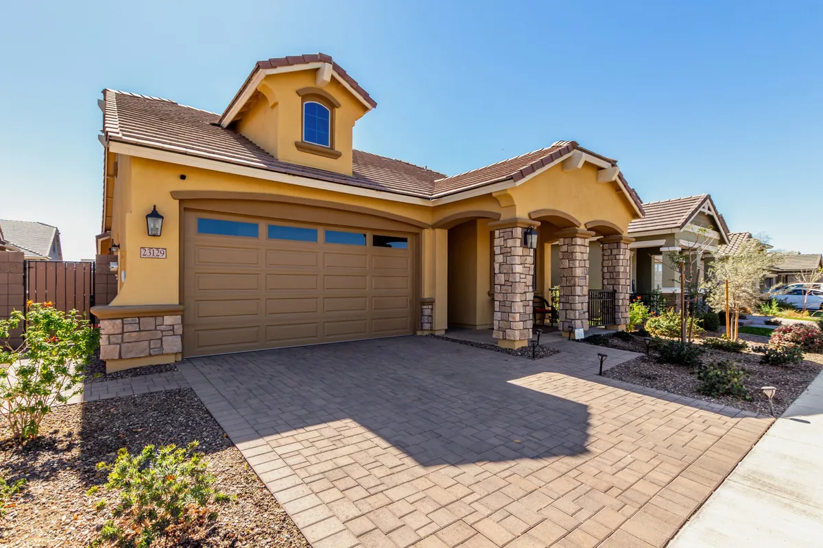 A beautifully landscaped front yard with a spacious driveway, stone accents on the house, and a cozy porch. The well-maintained greenery and inviting porch suggest a safe and welcoming neighborhood, perfect for evening strolls or relaxing outdoors.