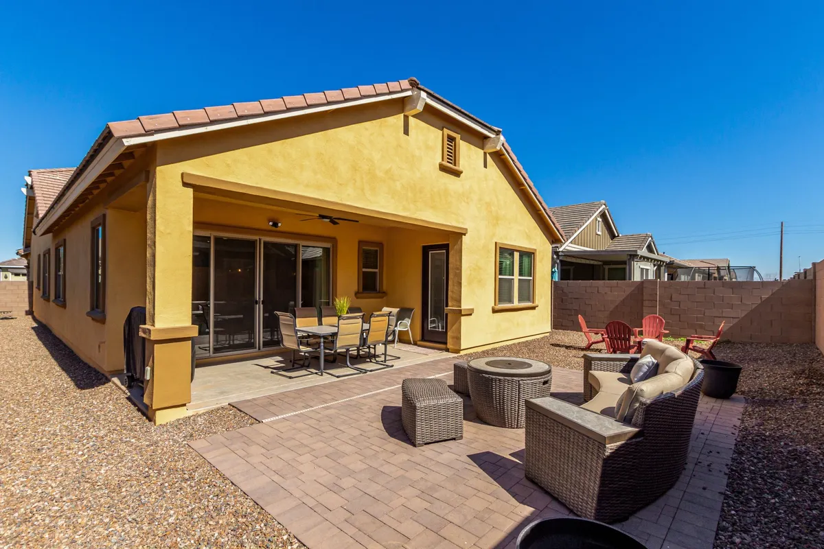 A stylish backyard patio setup with comfortable patio furniture, a dining table, and a cozy fire pit, framed by the home’s exterior. The scene is set for outdoor dining, relaxation, or social gatherings, with sunset views enhancing the ambiance.
