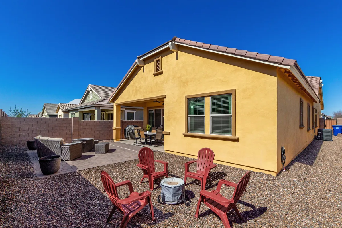 The backyard patio is set with red Adirondack chairs around a fire pit, creating a welcoming spot for social outdoor gatherings. The house exterior is visible in the background, and the mood suggests cozy evenings spent with friends or family.